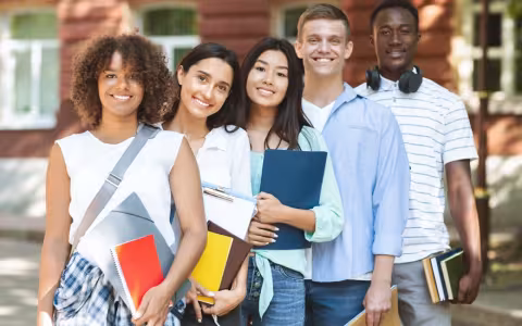 Multiethnic group of students standing near college building, posing at camera and smiling