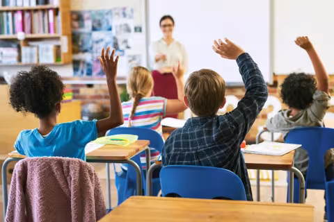 Smiling teacher applauding young student in classroom