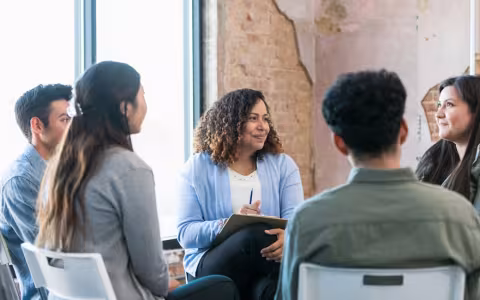 The diverse therapy group listens attentively as the young adult woman shares.