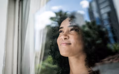Young woman looking through window at home