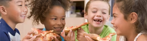 Four children laughing together while eating slices of pizza.